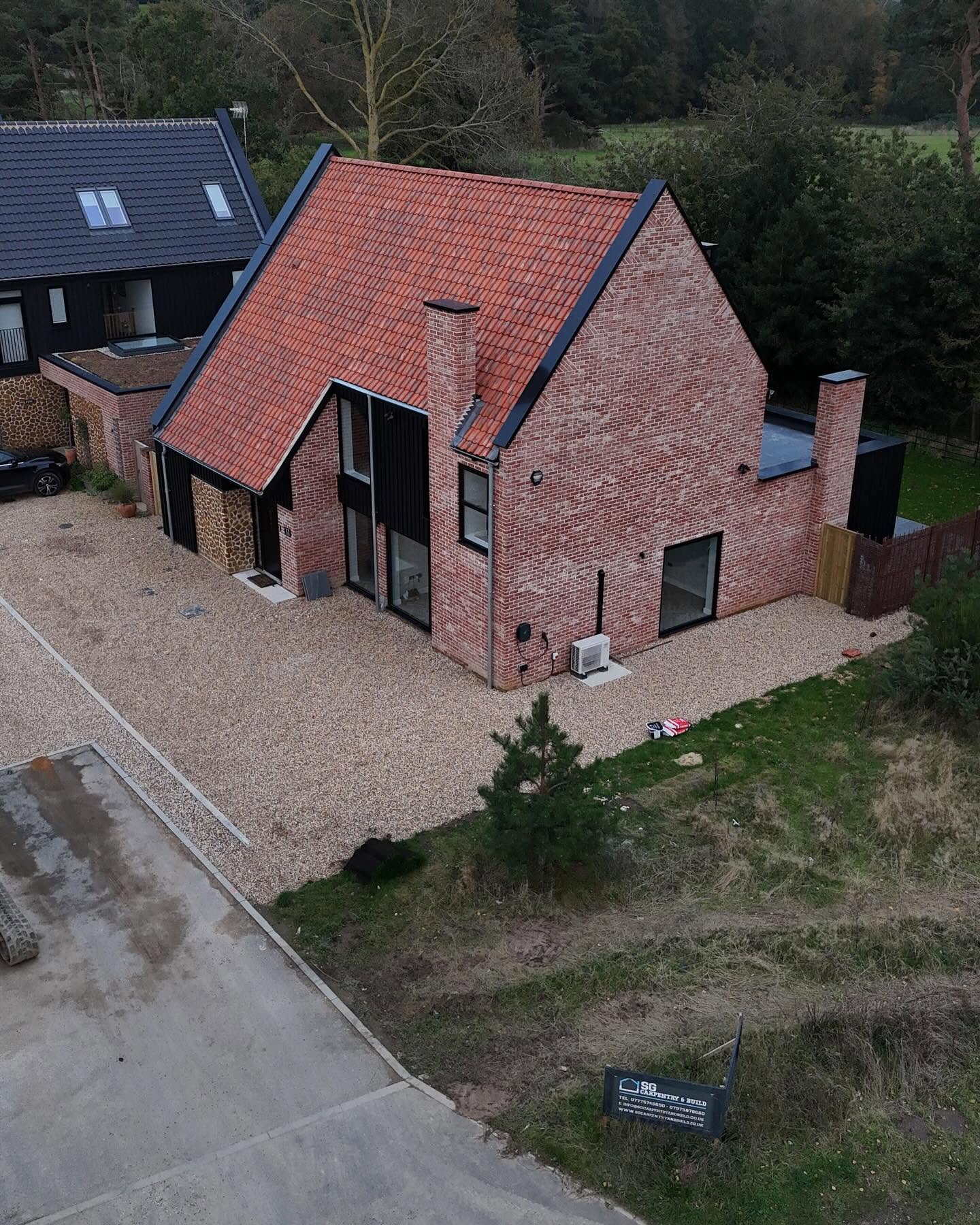 Aerial view of a completed new build in soft red brick, carstone panels and black cladding